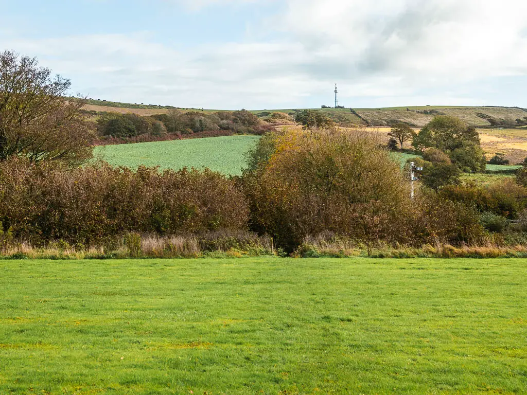 Looking across an immaculate grass field, to some bushes on the other side and a hill ahead in the distance. 