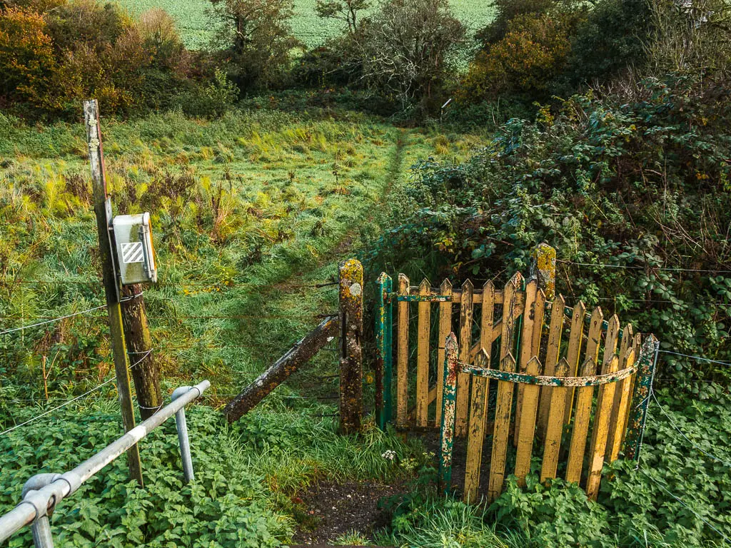 A wooden curved gate leading to a field with messy unkept grass.