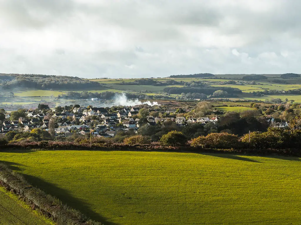 Looking down from the Purbeck Ridgeway to the fields and cluster of houses below, when walking between Corfe Castle and Swanage. 