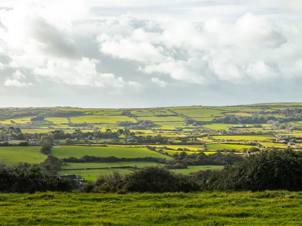 Looking across a vast expansion of green grass fields on the walk between Corfe Castle and Swanage along the Purbeck ridge. the fields are like patchwork lined with trees.