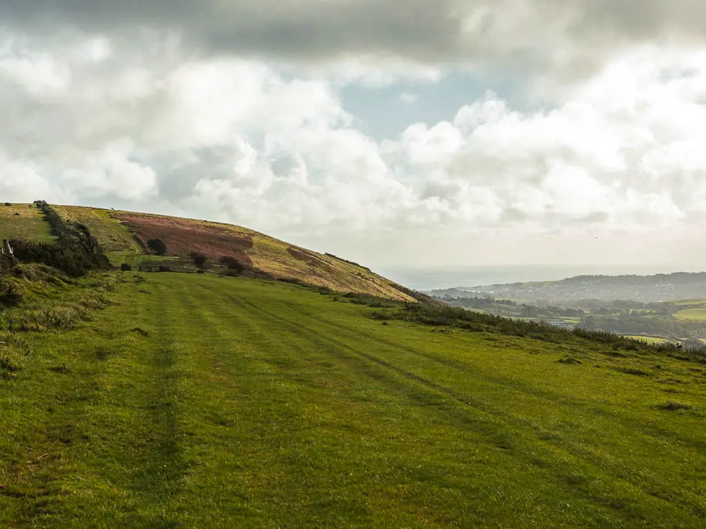 The grassy ridgeway which runs between Corfe Castle and Ballard Down. There is a hill along the ridge ahead, and view to the sea in the distance. 