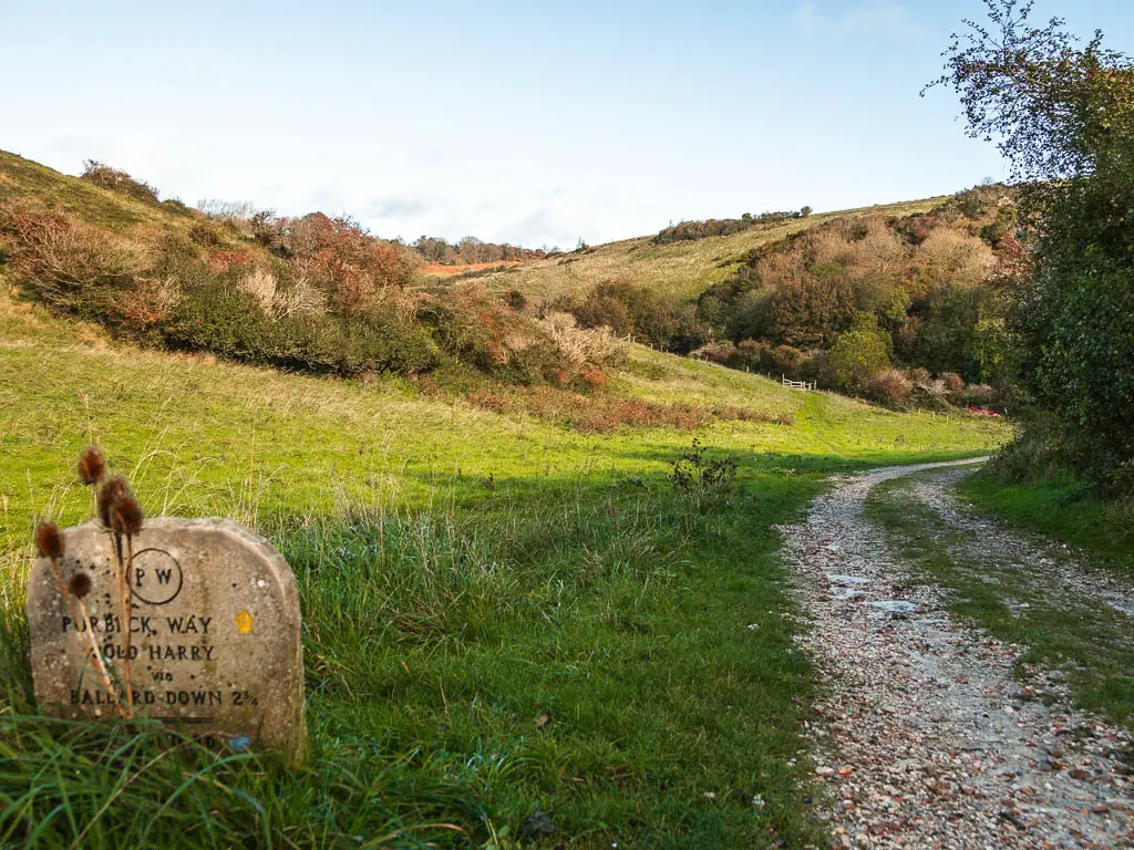 A stone trail sing on the grass on the left side of a gravel path, with underling hills ahead. 