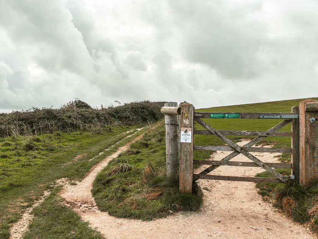 A wooden gate with a trail leading along the left side of the fence.