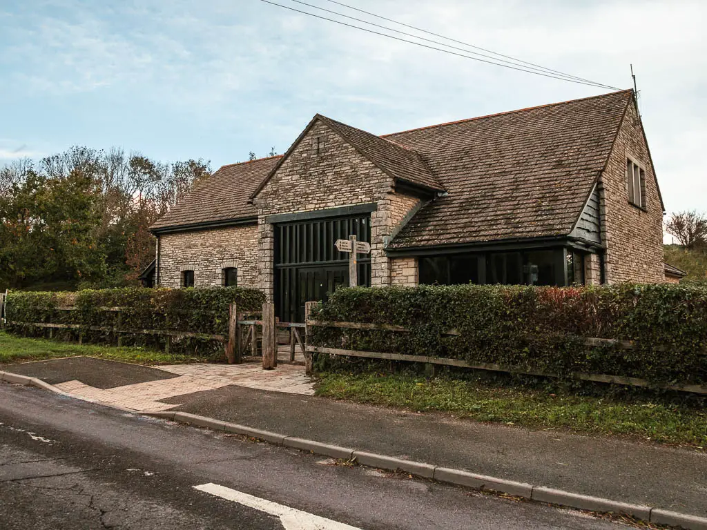 Looking across the road to the stone building of the Corfe Castle National Trust centre. There is a green hedge in front of the building.