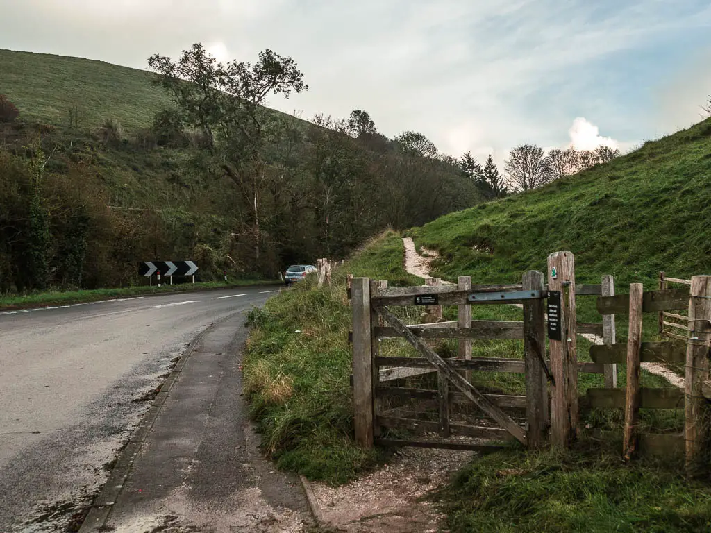 A road on the left, and wooden fence leading onto a trail up the hill on the right.