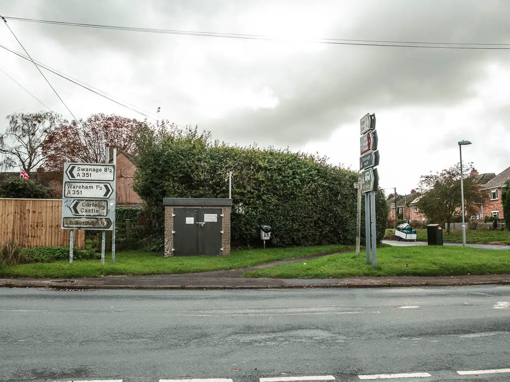 Looking across the road, to a green verge on the other side with various road signs.