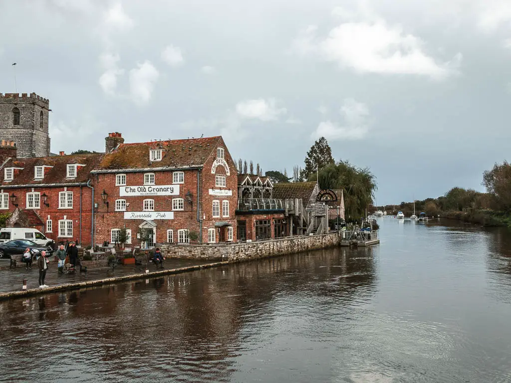 Looking across the rirver from in Wareham, at the start of the walk to Corfe Castle. There are bring and stone buildings on the left side of the river.