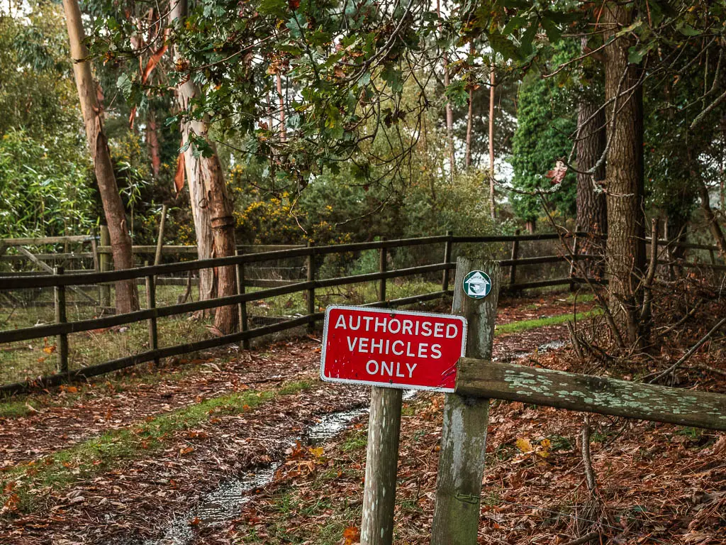 A red sign saying 'authorised vehicles only' and a green trail arrow pointing ahead on the wooden fence next to it. 