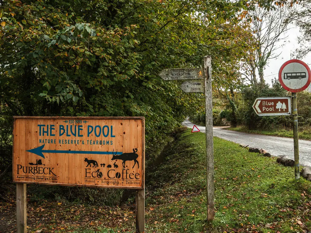 A big wooden sign pointing left to walk to the blue Pool. There is a wooden trail sign on the right of it, pointing left to walk to Corfe Castle.