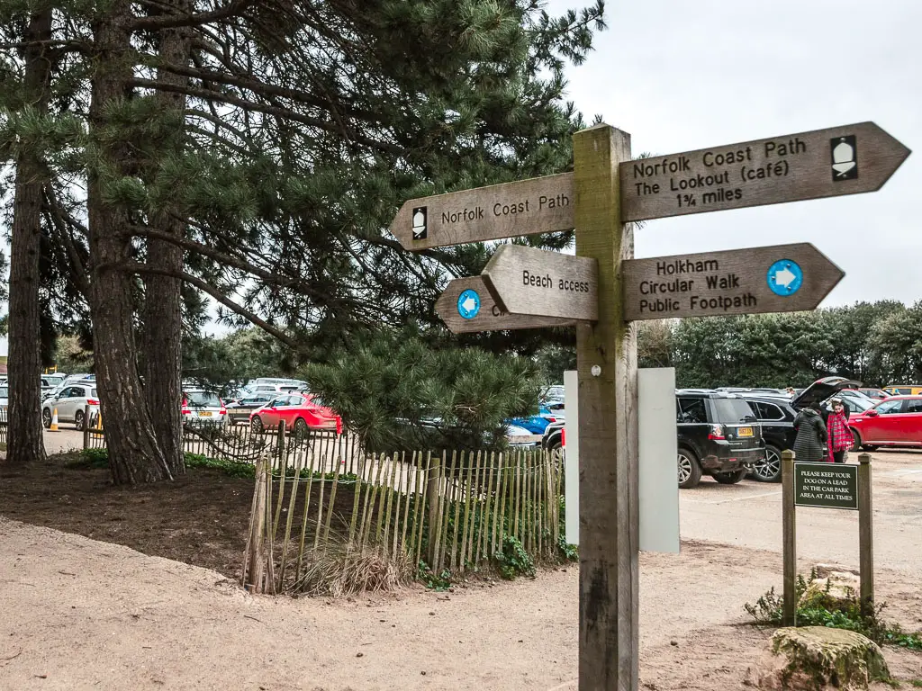 A wooden trail signpost pointing in all directions, with the full car park behind.