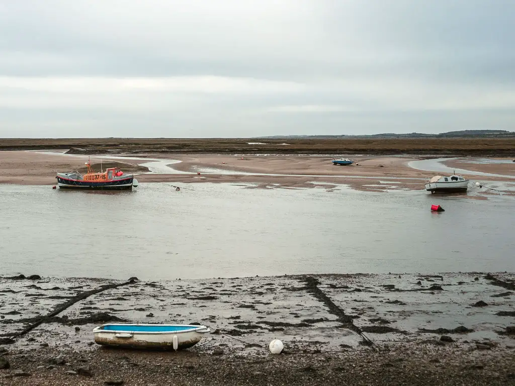 Two small boats sitting on the low river, and one small row boat on the river bed, halfway through the walk between Burnham Overy Staithe and Blakeney.