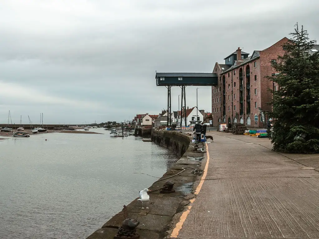 A walkway on the right and river on the left. There is a tall brick building ahead on the right side. 