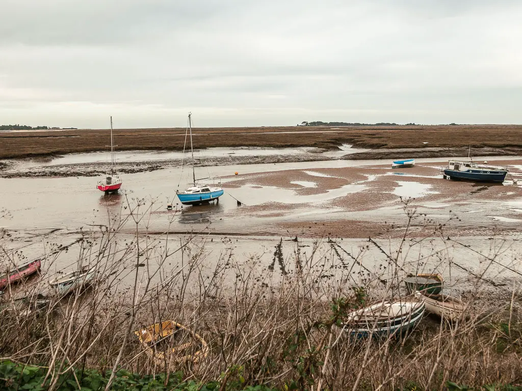 A few boats sitting on the river bed, with marshland on the other side, when walking from Burnham Overy Staithe to Blakeney. There is a mix of row boats and sailing boats.