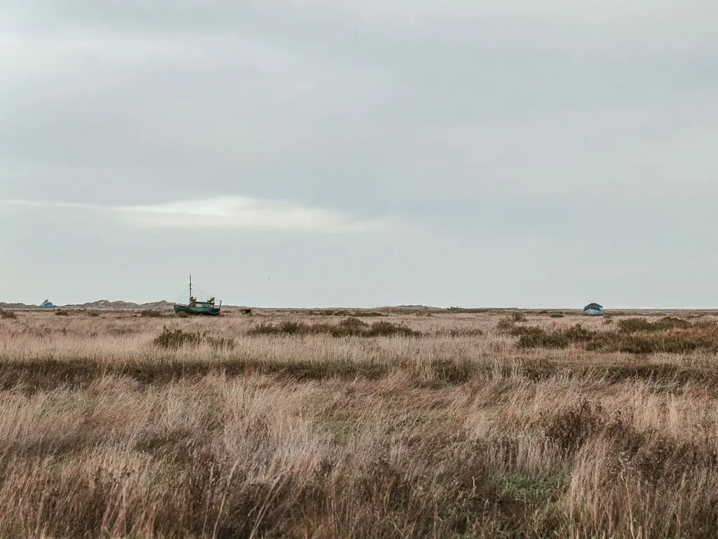 Looking across the beige coloured marshes on the walk between  Burnham Overy Staithe and Blakeney. There is a boat moored in the distance.