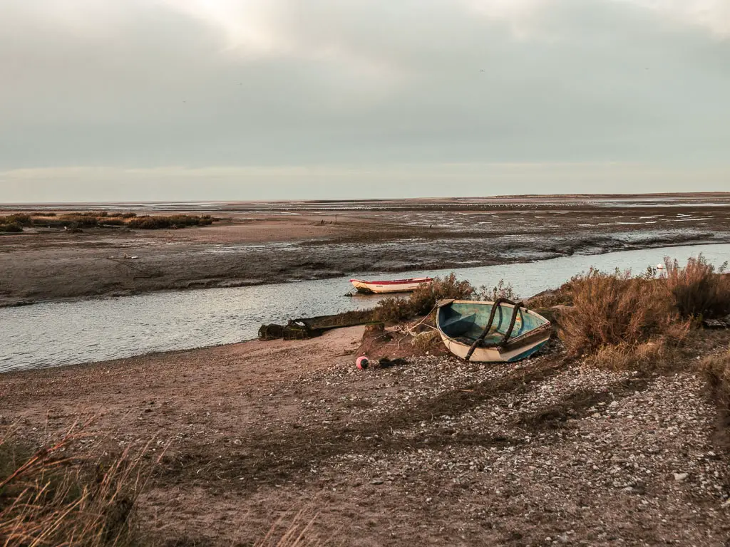 A small row boat sitting on the rocky bank next to the river, on the walk from Burnham Overy Staithe to Blakeney.