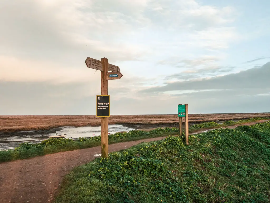 A wooden trail sign point on the ridge path. There is green grass down the side of the ridge.