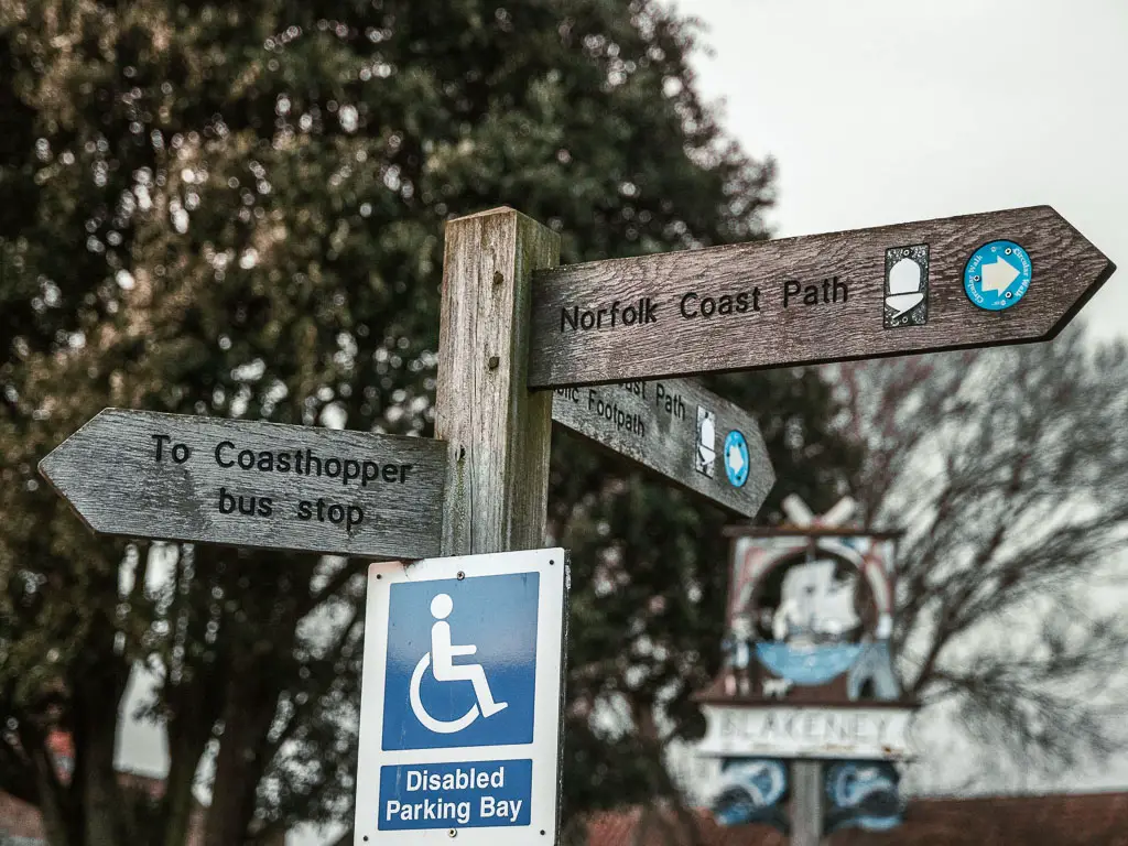 A wooden trail signpost pointing towards to bus stop and Norfolk coast path.