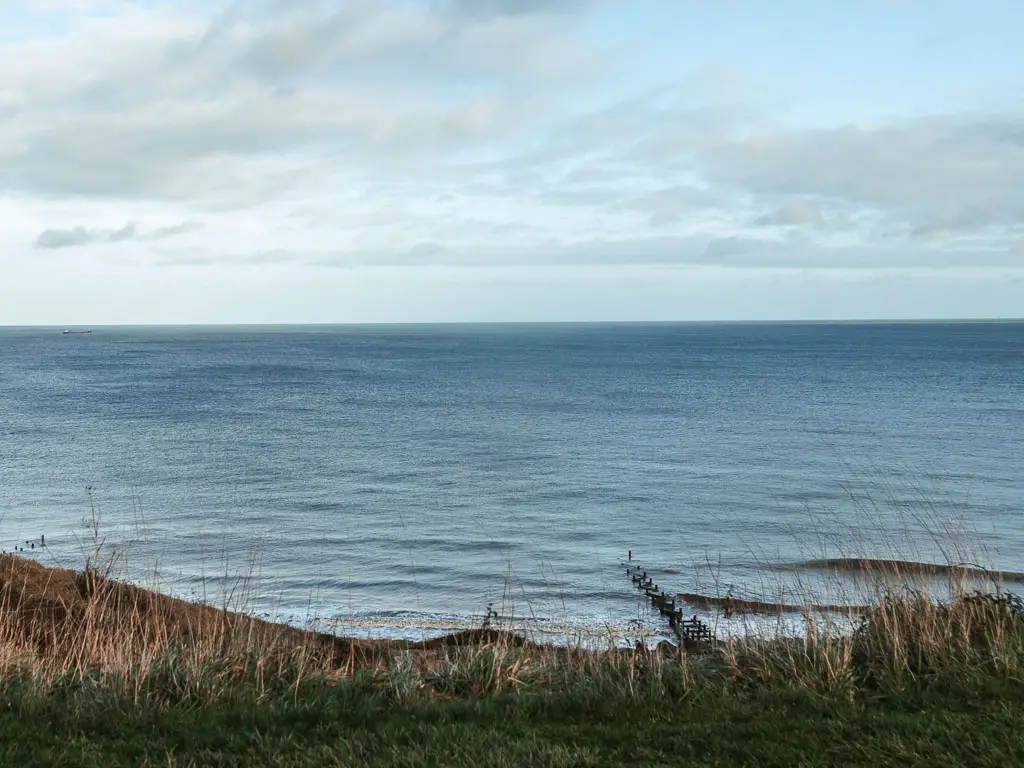 Looking down the grass hill to the blue sea below.