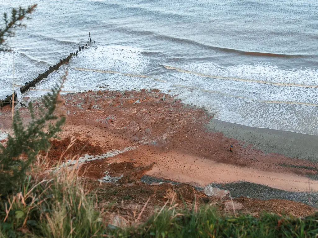 Looking down to the beach below as it meets the sea, along the walk from Cromer to Mundesley. There are two people barely visible walking along the beach.