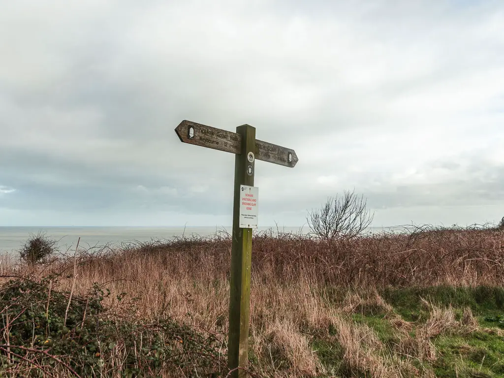 A wooden trail signpost pointing ahead and back, surround by hay and grass.