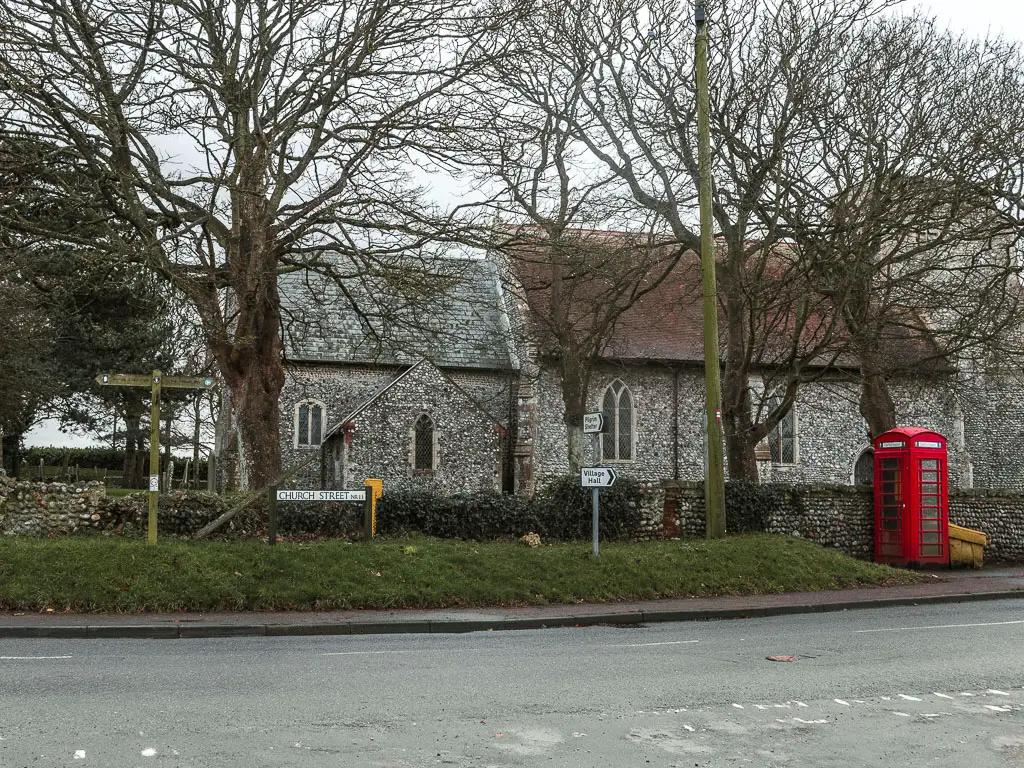 Looking across the road, to a church and red telephone box on the other side, partway through the walk from Cromer to Mundesley.