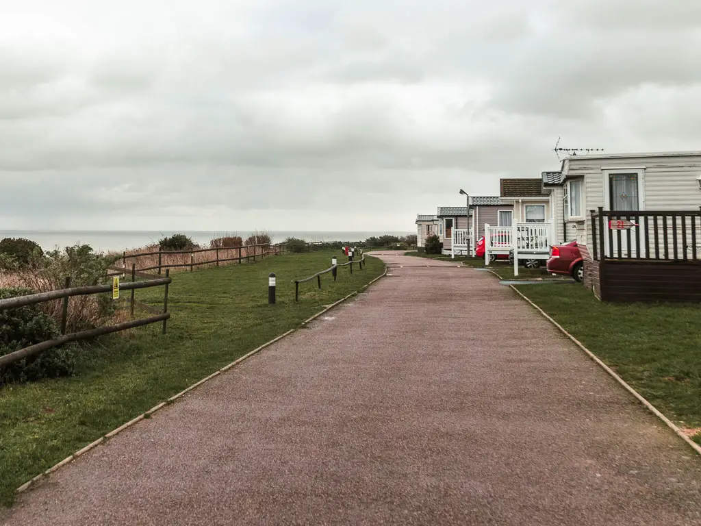 A wide walking path, lined with a strip of grass on the left, and caravan holiday homes on the right.