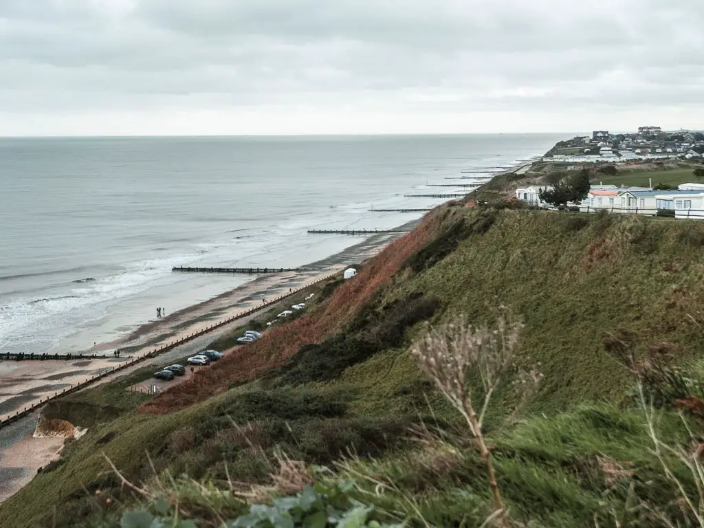 Looking down the grassy cliffside to the beach and sea below on the left, part way through the walk from Cromer to Mundesley. There are holiday homes all along the clifftop ahead.