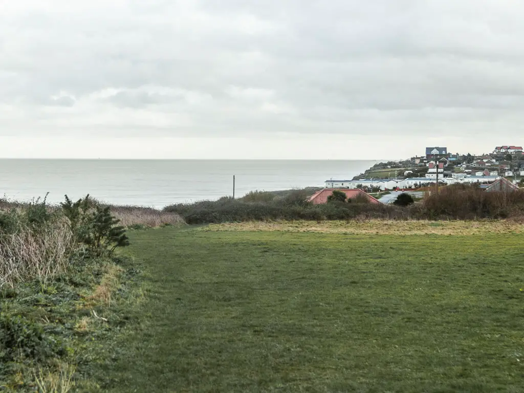 A large green, with rooftops visible ahead on the right, and the sea on the left.