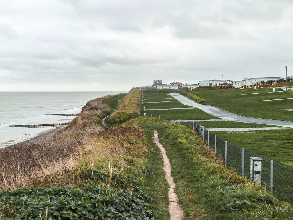 A thin trail leading along the grass clifftop when walking from Cromer to Mundesley. The sea below to the left and a large area of grass to the right.