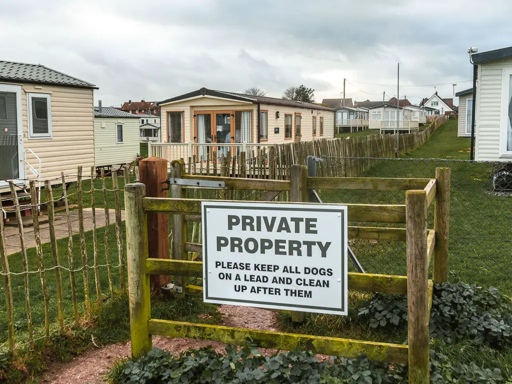 A big white sign saying 'private property' on a wooden fence and gate, with caravan park holiday homes on the other side.