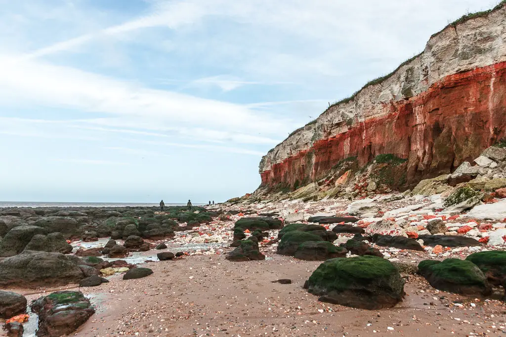 The red and white Hunstanton cliffs looming above on the right, above a beach of sand with big rocks, on the walk towards Burnham Overy Staithe.