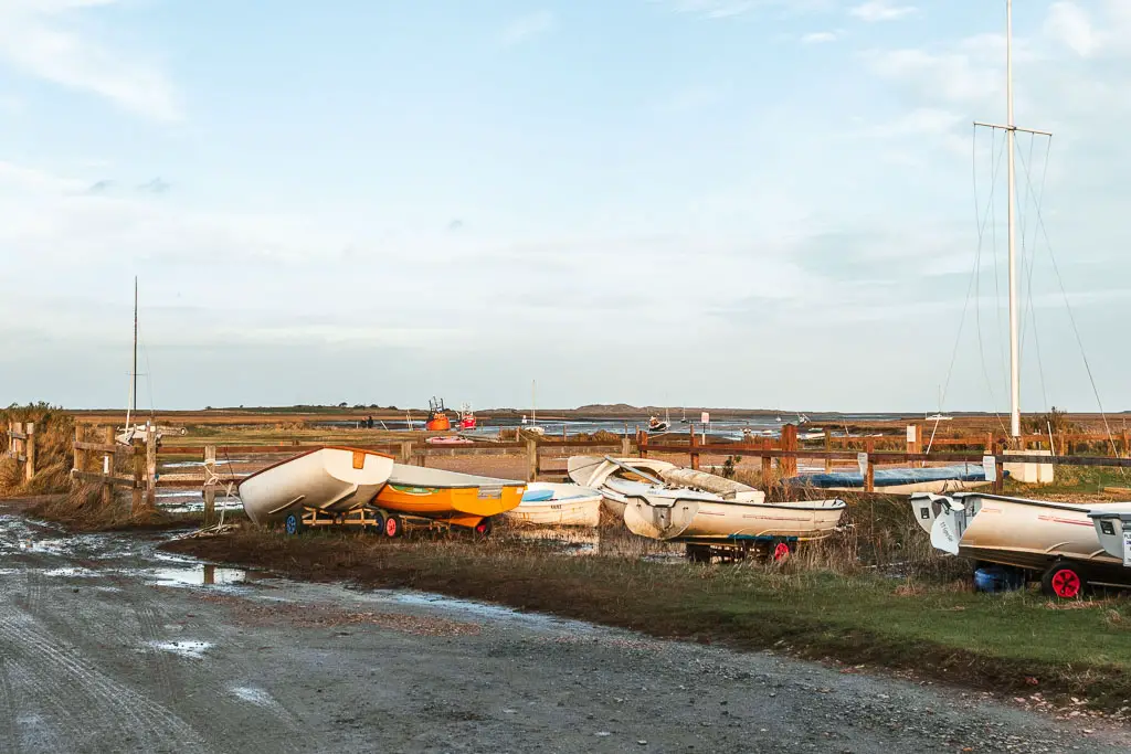 Looking across the road with lots of small boats sitting on the grass, and the marshes in the distance. 