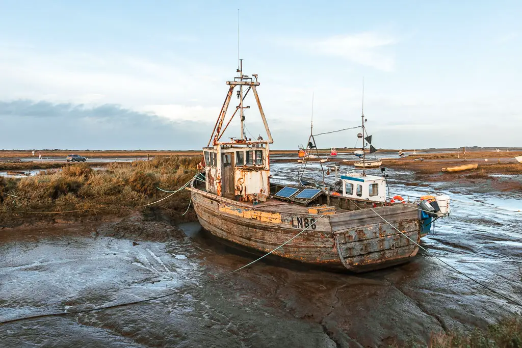 A fishing boat sitting on the black mud river bed, with the marshes behind, on the walk from Hunstanton to Burnham Overy Staithe.