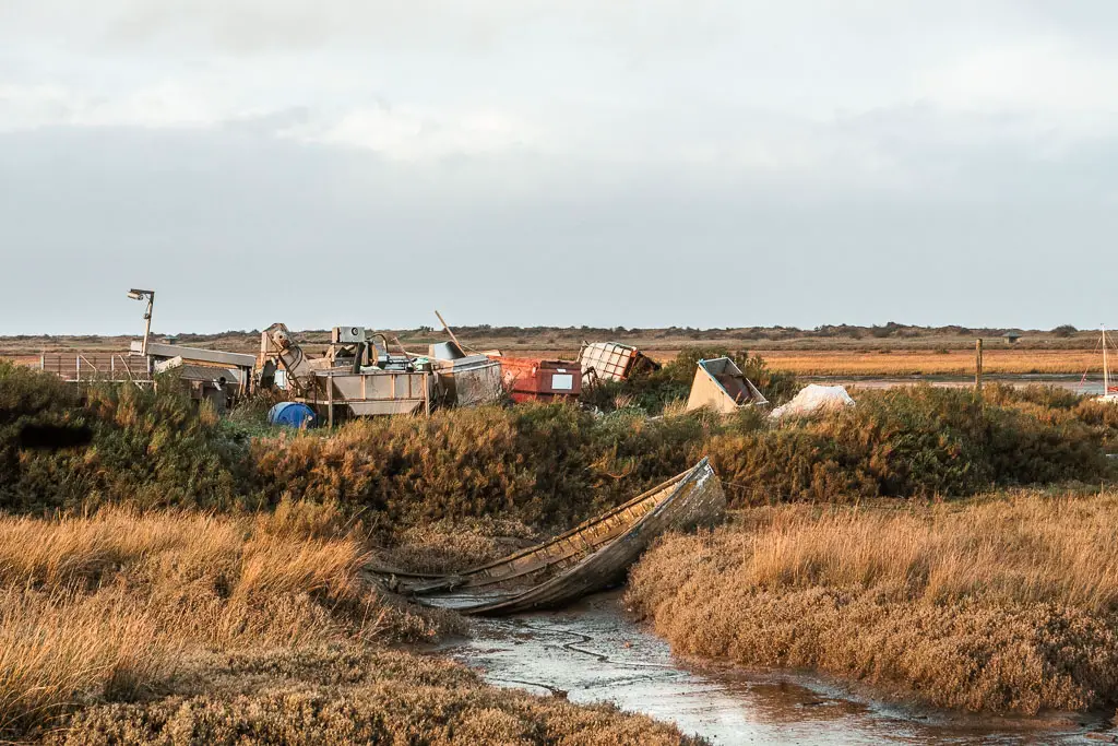 The marshes with a small stream, and the ruins of a row boat resting half on the stream half in the marshes, on the walk from Hunstanton to Burnham Overy Staithe.