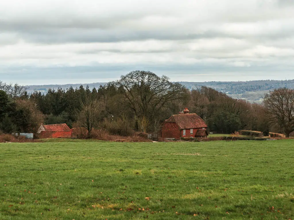 Looking across a large grass field, to a cottage on the other side, when walking from Oxted to Otford. There are trees behind the cottage.