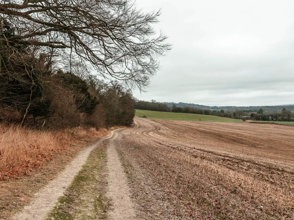 A trail leading ahead, on the left side of a large field, near the start of the walk from Oxted to Otford. 