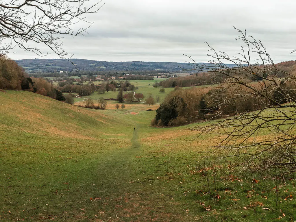 Looking down through a dip in the hill to a view of the fields and trees in the distance, near the end of the walk from Oxted to Otford. 