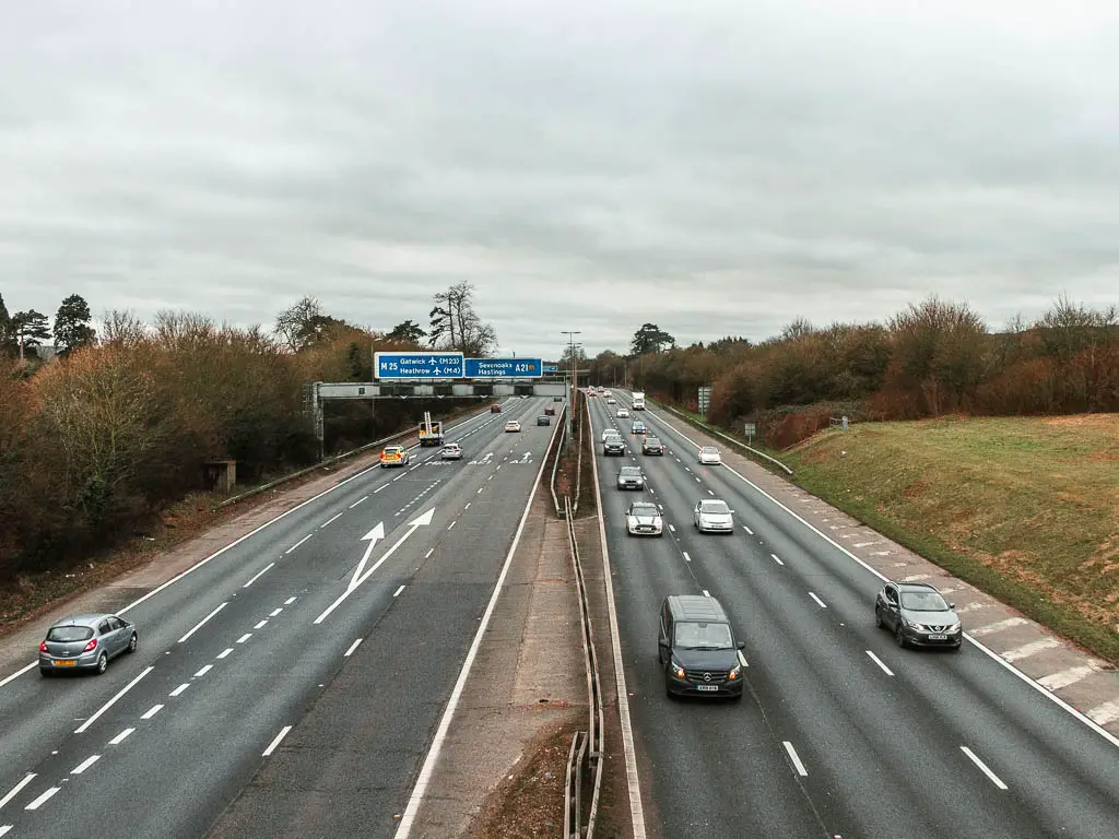 Looking down along the M25, as it runs straight ahead. There are lots of cars driving along it.