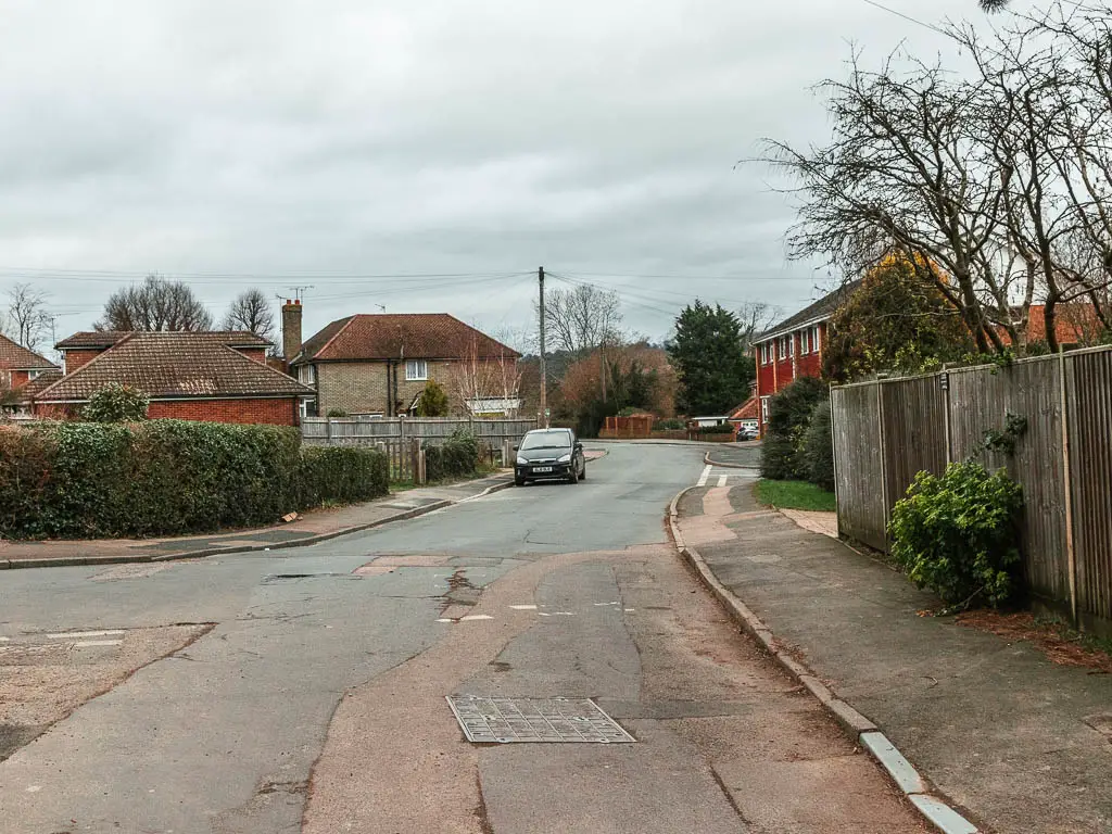 Looking along a residential road lined with houses. There is a parked car ahead.