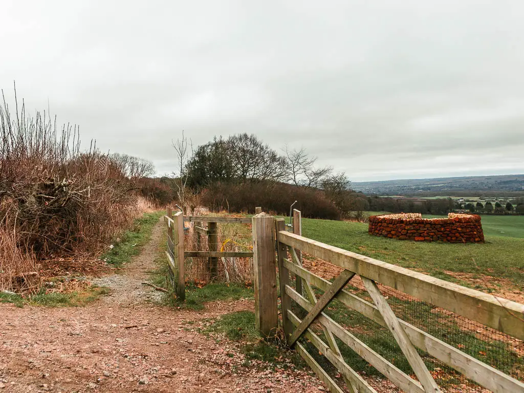 A gravel path leading g ahead, with a wooden fence and grass field to the right. 