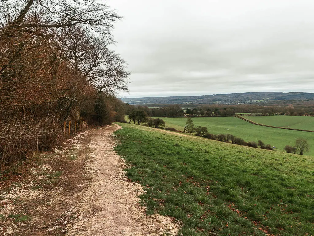 A path leading ahead on the right, at the top of a green grass field, with views to the fields in the distance on the right, when walking from Oxted to Otford.