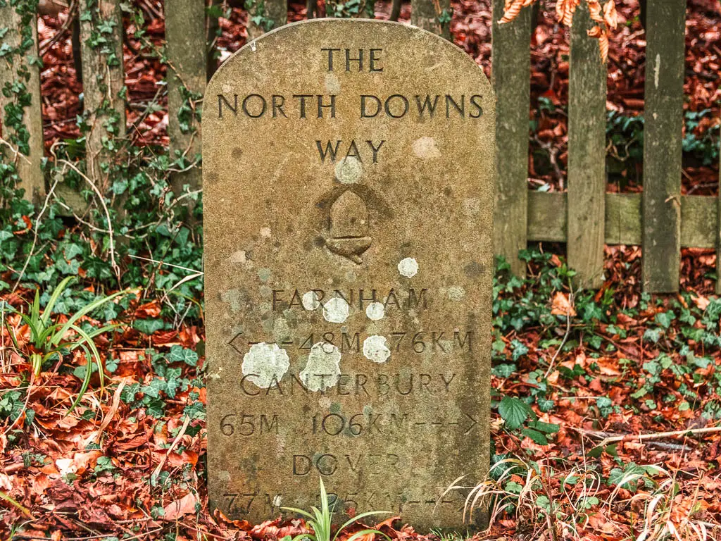 A stone plaque marking the North Downs Way, pointing left for Farnham, and right for Canterbury and Dover.