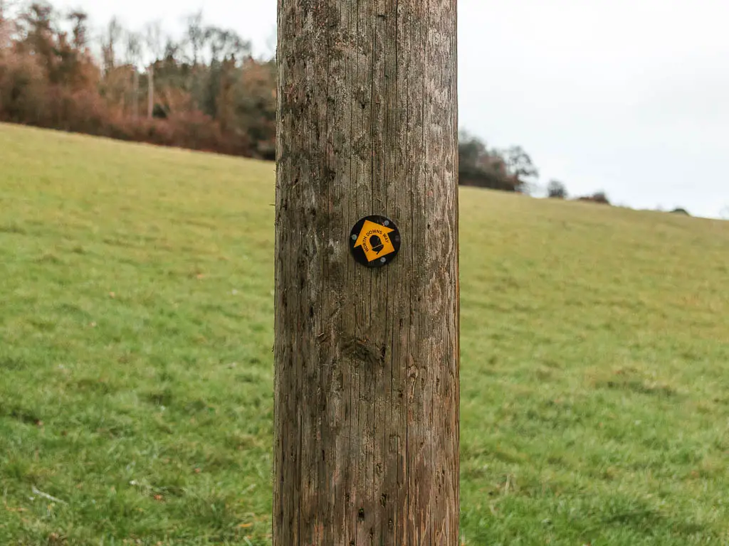 A wooden pole with a yellow arrow sign pointing up the hill.