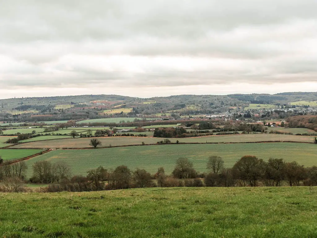 Looking down the grass hill to a vast view of patchwork green field as far as the eye can see, partway through the walk from Oxted to Otford.