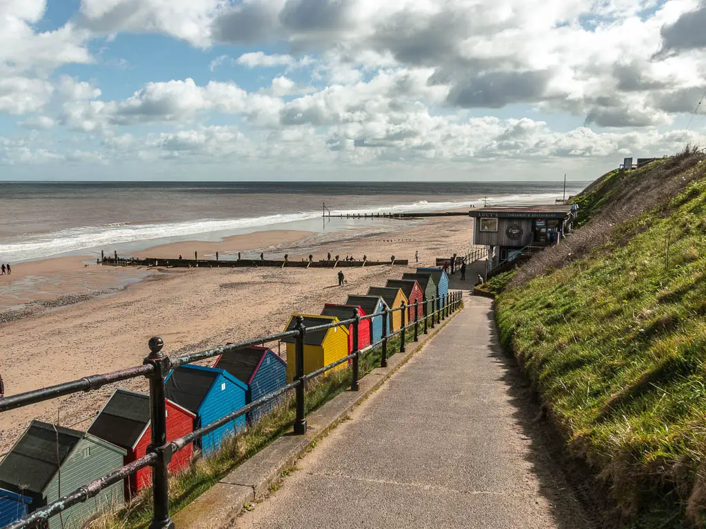 A walking path leading down to the beach, with colourful beach huts on the edge.