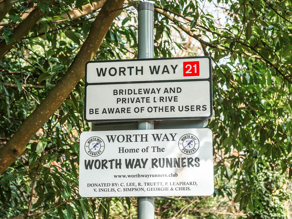 A white sign on a post saying Worth Way. The sign is in front of a green leafy tree.