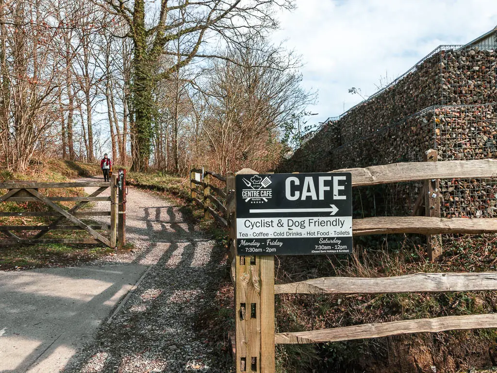 A black and white sign for a cafe, on a fence, with the walking trail leading past it on the left.