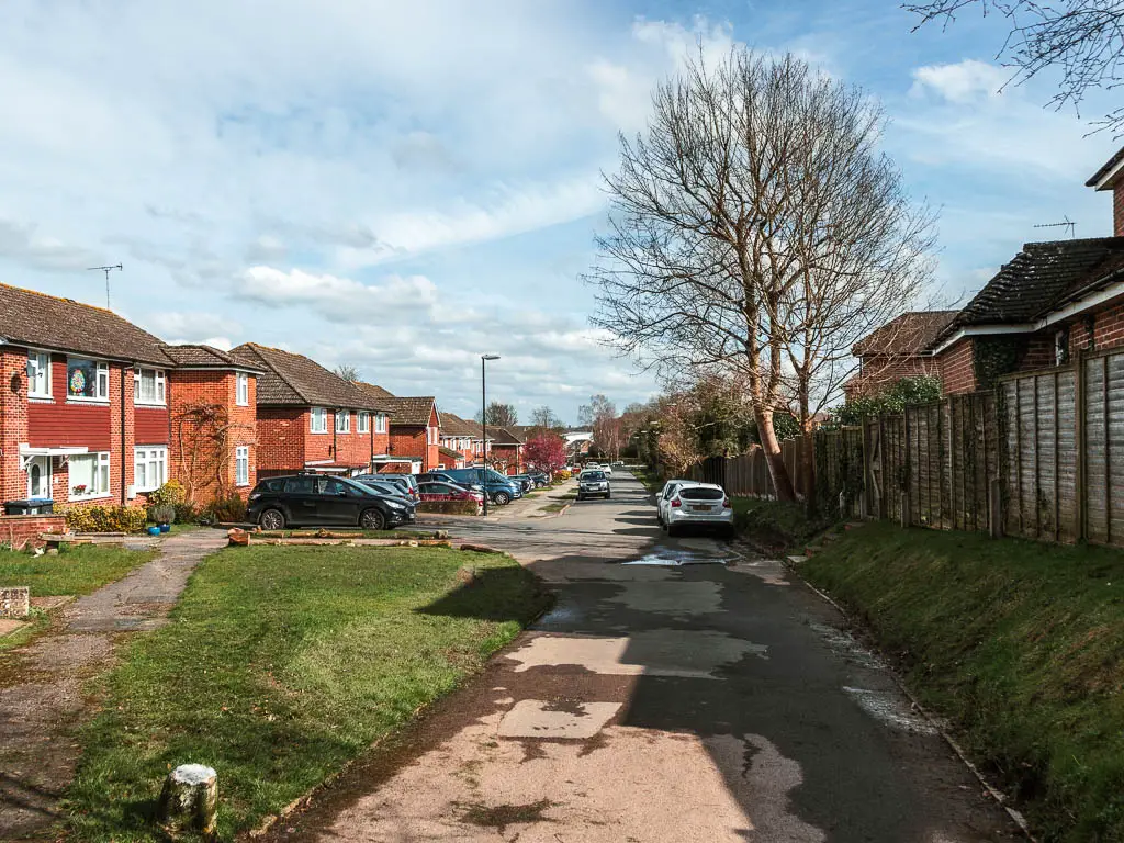 A residential road lined with houses, and parked cars.