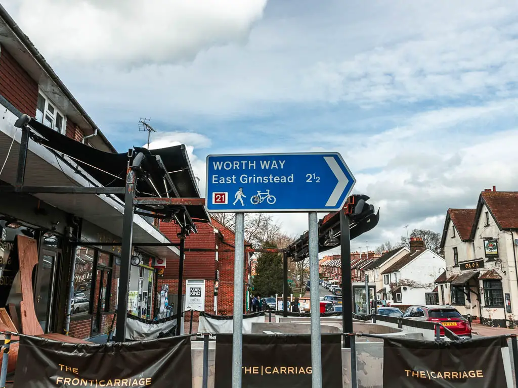 A blue sign pointing right to walk the worth way towards east grinstead. The sign is in front of a restaurant in the town centre.