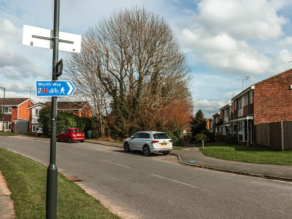 A blue arrow sign on a black lamppost pointing to a path between the houses across the road for the Worth Way trail.